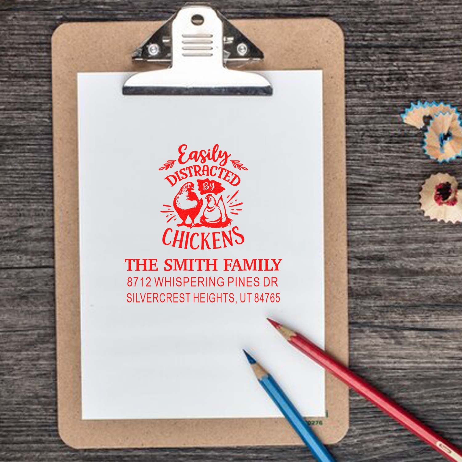 Custom family address stamp with Easily Distracted by Chickens design on a clipboard, with pencils on a rustic wood desk.