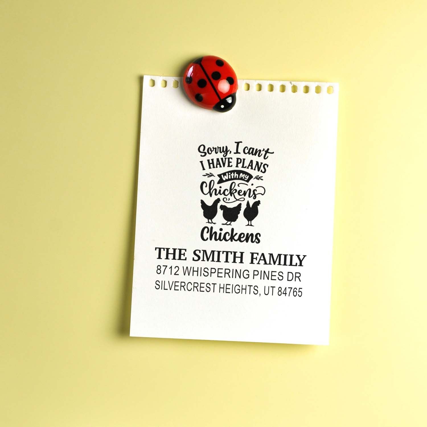 Custom chicken-themed address stamp sample on white paper, clipped with a red ladybug magnet against a pale yellow background.