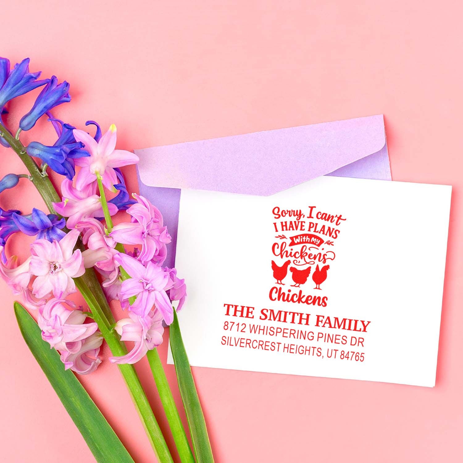 Custom chicken return address stamp on a white envelope with pink and purple flowers against a pastel pink background.