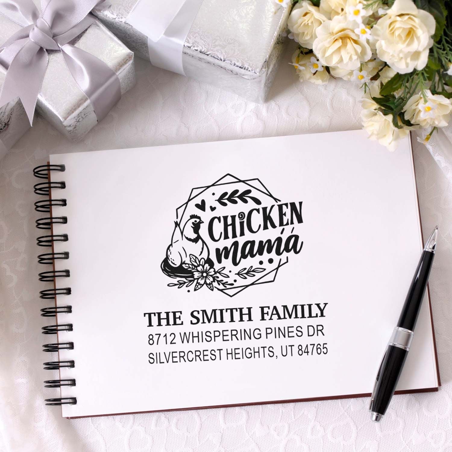Custom chicken mama address stamp on spiral notebook, surrounded by silver gift boxes, flowers, and pen for farmhouse stationery branding.