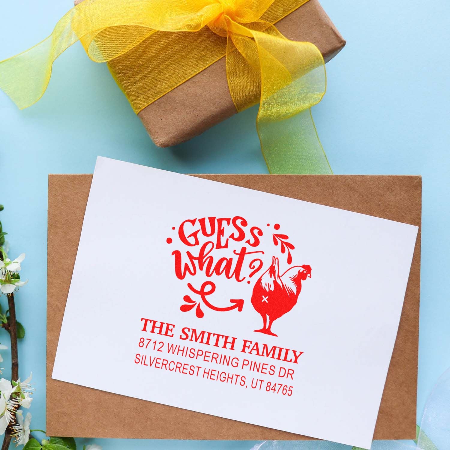 Custom return address stamp with Guess What? chicken design on a gift card, beside a wrapped present on a blue background.