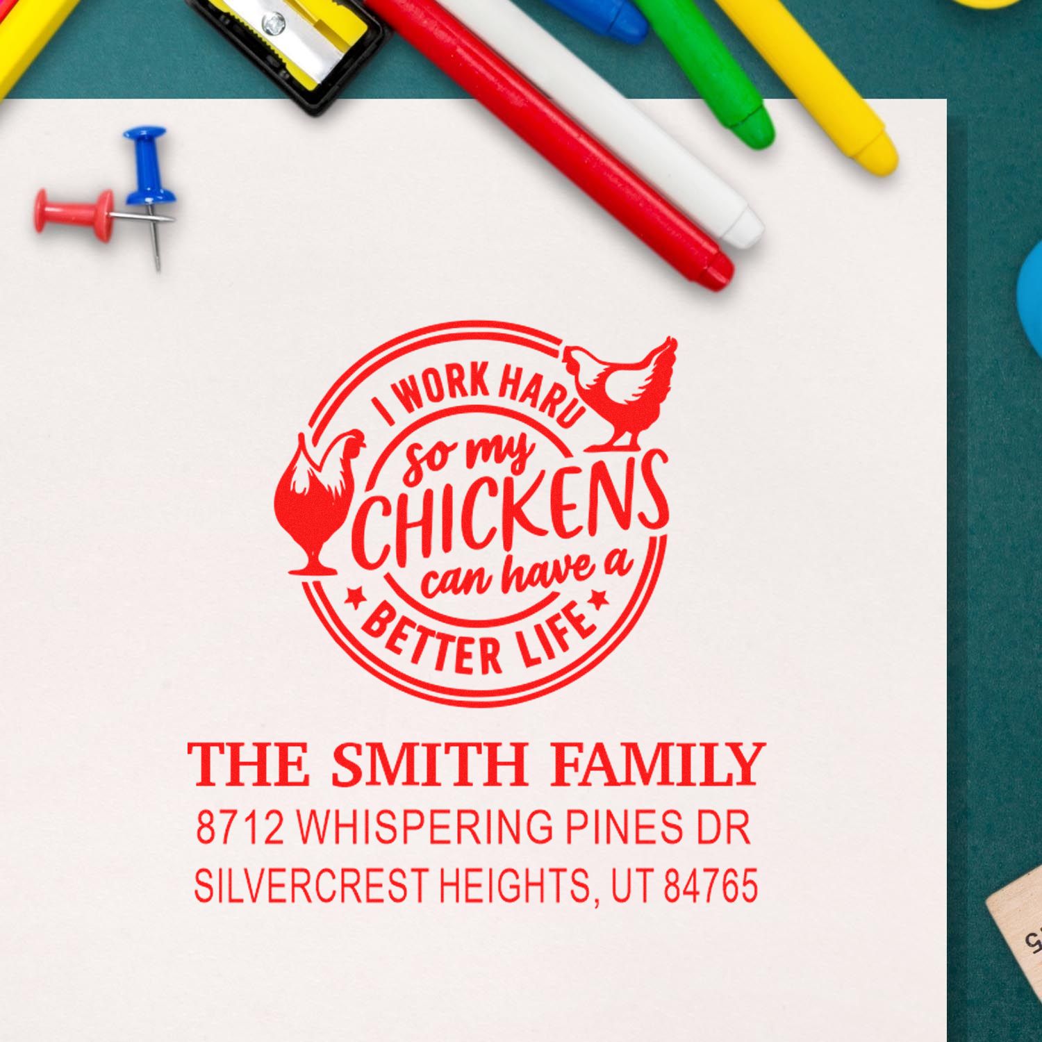 Custom chicken-themed family address stamp imprint in red on white paper, surrounded by colorful pens and push pins on a desk.