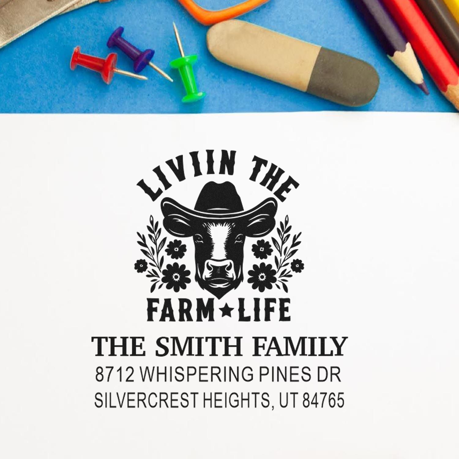 Custom farm life address stamp with cow and cowboy hat design on white paper, shown with pencils, push pins, and eraser on a desk.