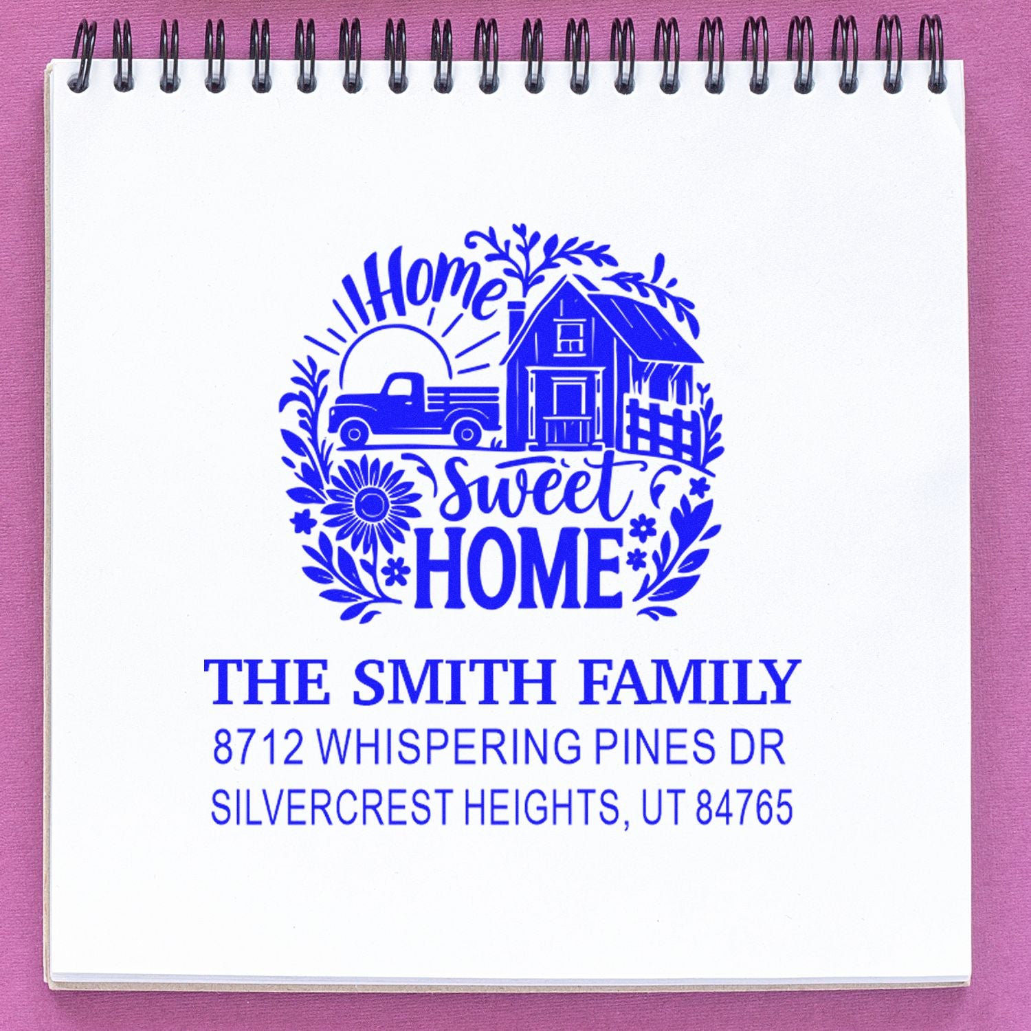 Custom Home Sweet Home personalized address stamp with farmhouse, truck and floral design stamped on a spiral notebook against a pink background.