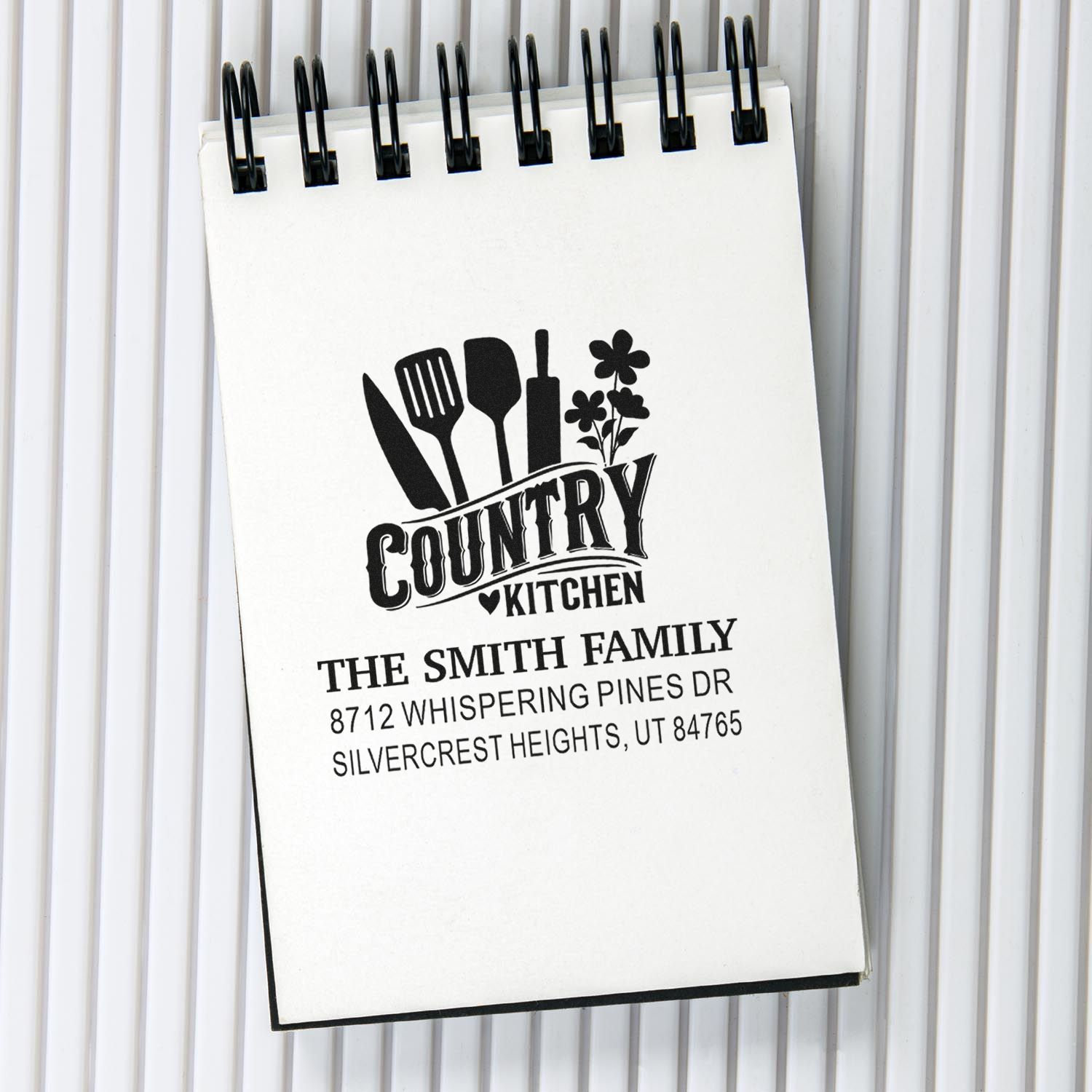 Custom family kitchen address stamp on a spiral-bound notepad, featuring utensils, flowers, and the Smith family name with Utah address.