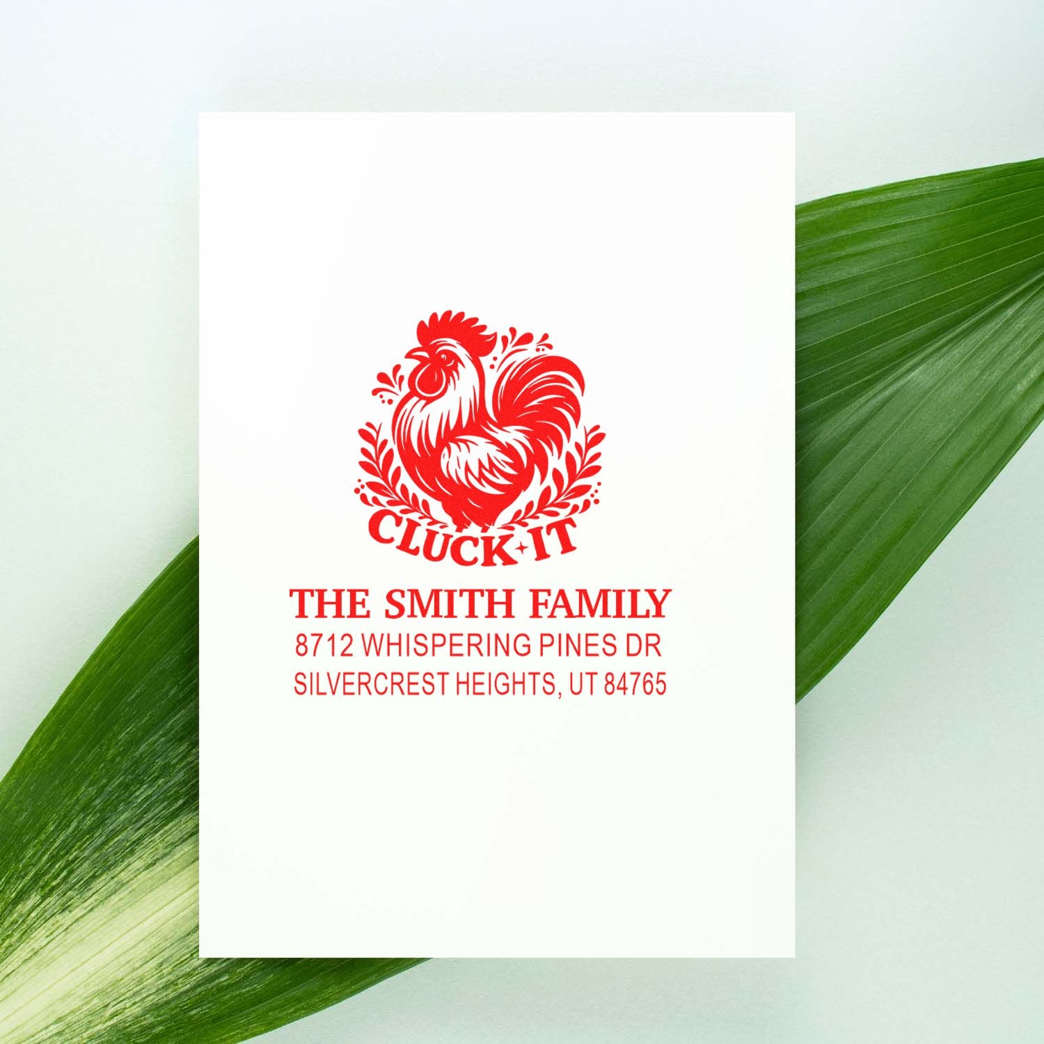 Custom red rooster address stamp for The Smith Family with Cluck It design, shown on a white card against green leaves.