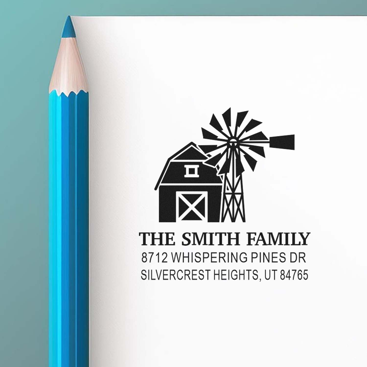 Custom family address stamp with barn and windmill design, beside a blue pencil on a white background.
