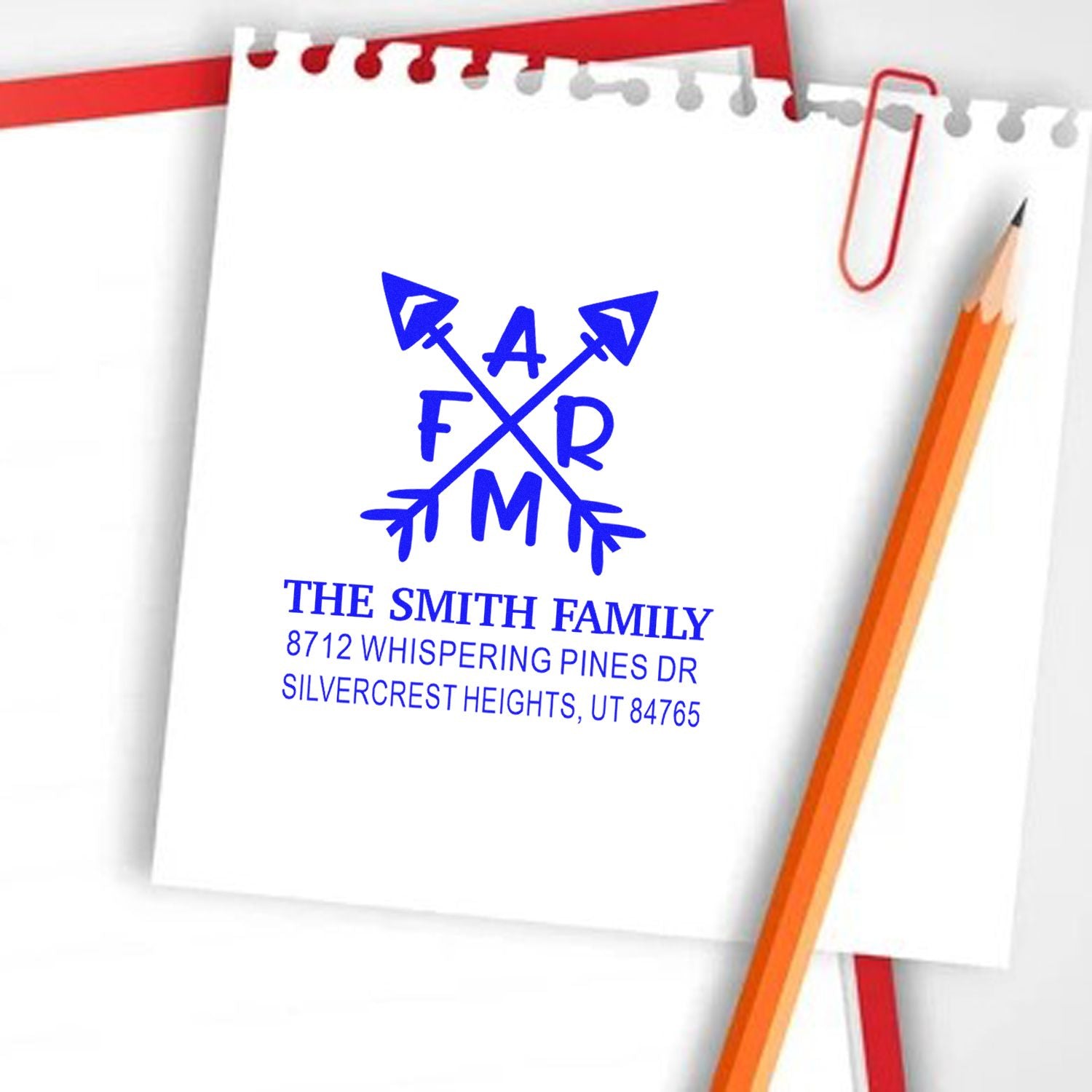 Personalized family return address stamp for The Smith Family, showing blue crossed-arrows monogram on a notepad with pencil and paper clip.