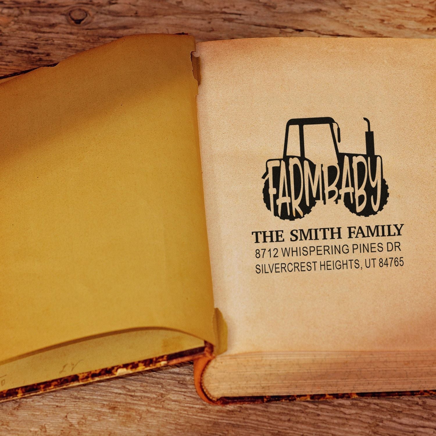 Personalized farmhouse tractor address stamp with The Smith Family name and Utah address on an open book over a rustic wood table.