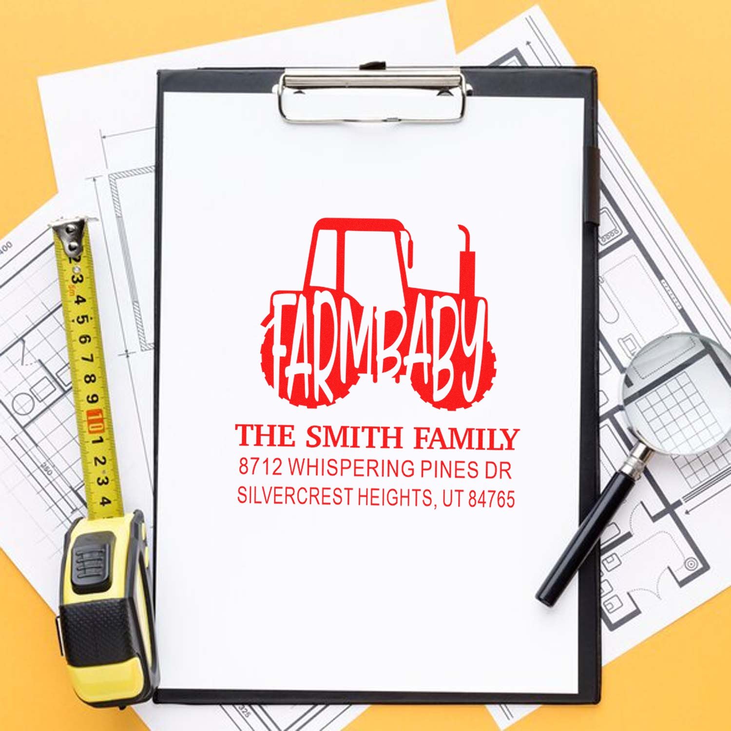 Custom farm tractor address stamp on clipboard with blueprint plans, measuring tape and magnifying glass on yellow background.
