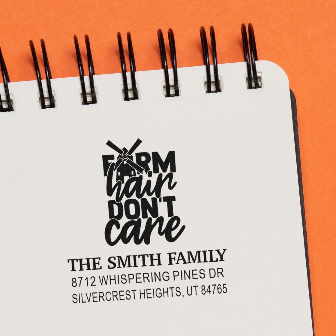 Custom family address stamp on a spiral notebook, reading Farm hair dont care, set against an orange background.