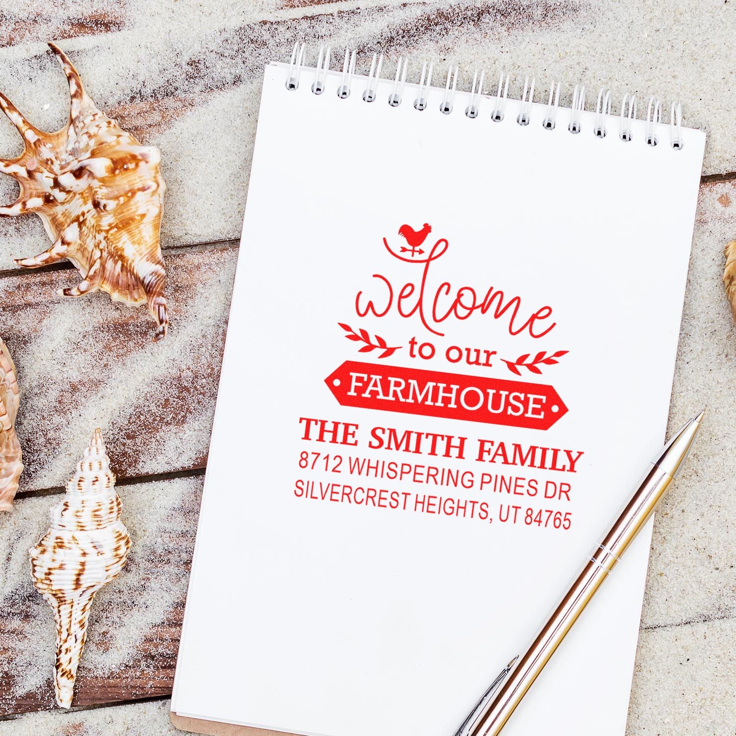 Personalized farmhouse welcome address stamp on a spiral notepad, styled with seashells and pen on a rustic beach surface.