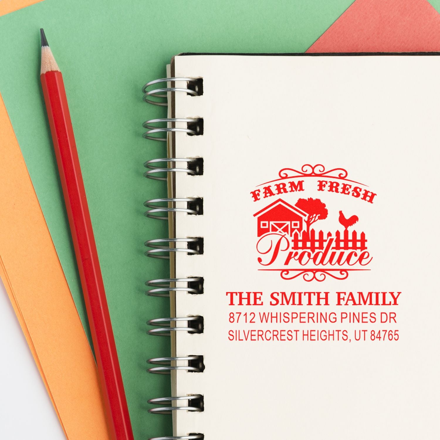 Custom Farm Fresh Produce address stamp on a spiral notebook, beside a red pencil and colorful paper backgrounds.
