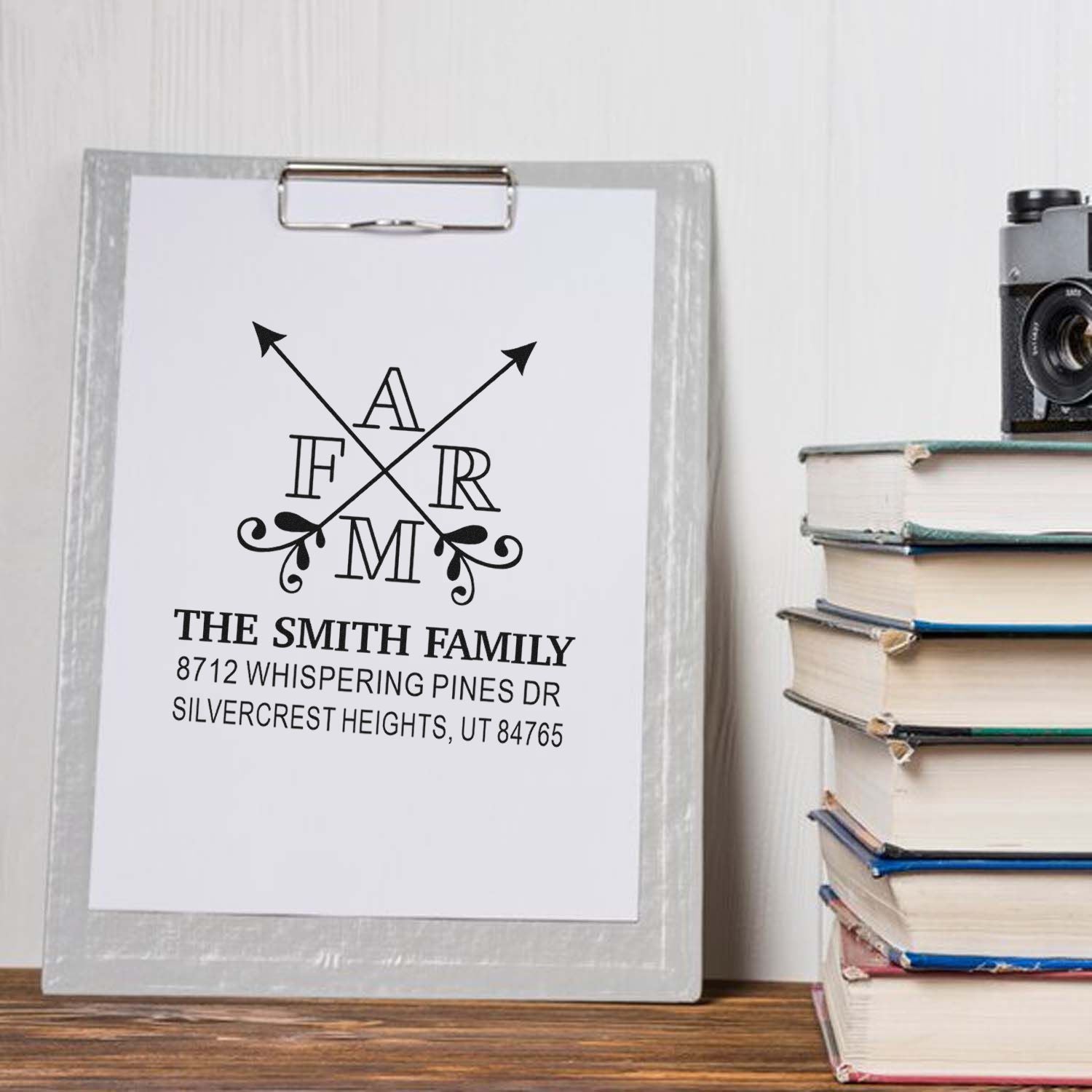 Personalized family address stamp on clipboard beside stacked books and a vintage camera on a wooden shelf.