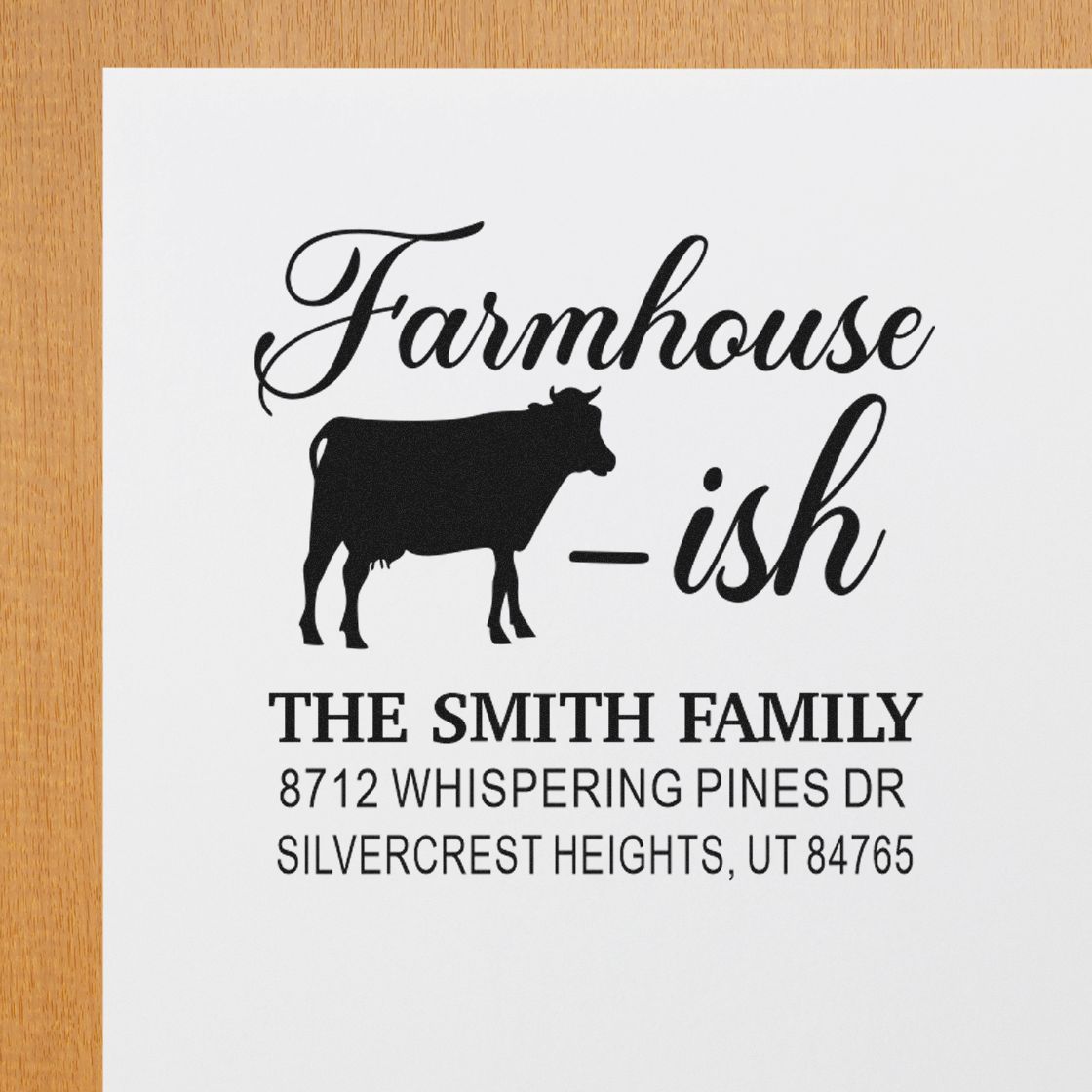 Custom farmhouse-style address stamp with cow silhouette, The Smith Family name, and Utah address on white paper over a wood table.