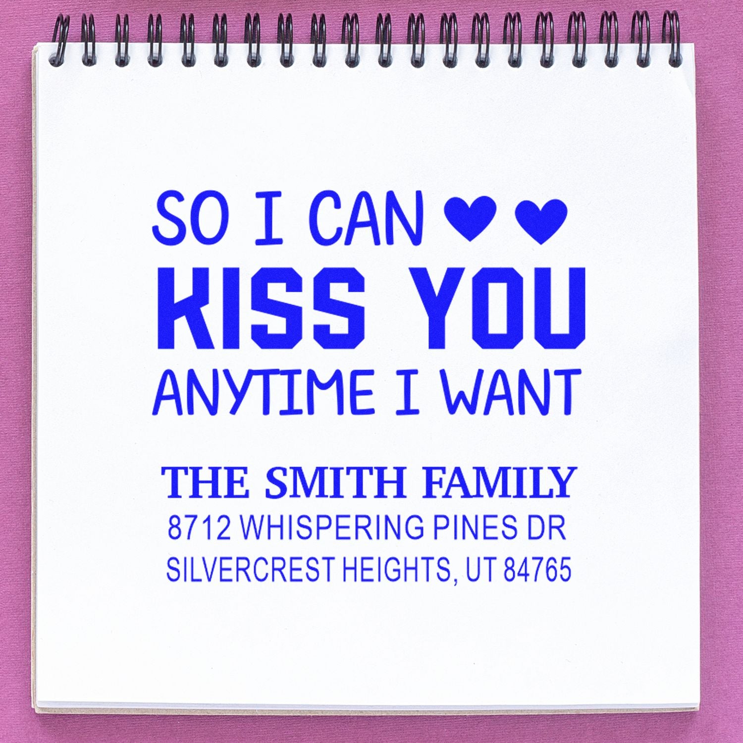 Custom address stamp on a spiral notebook, showing blue So I can kiss you anytime I want text with hearts and The Smith Family address.