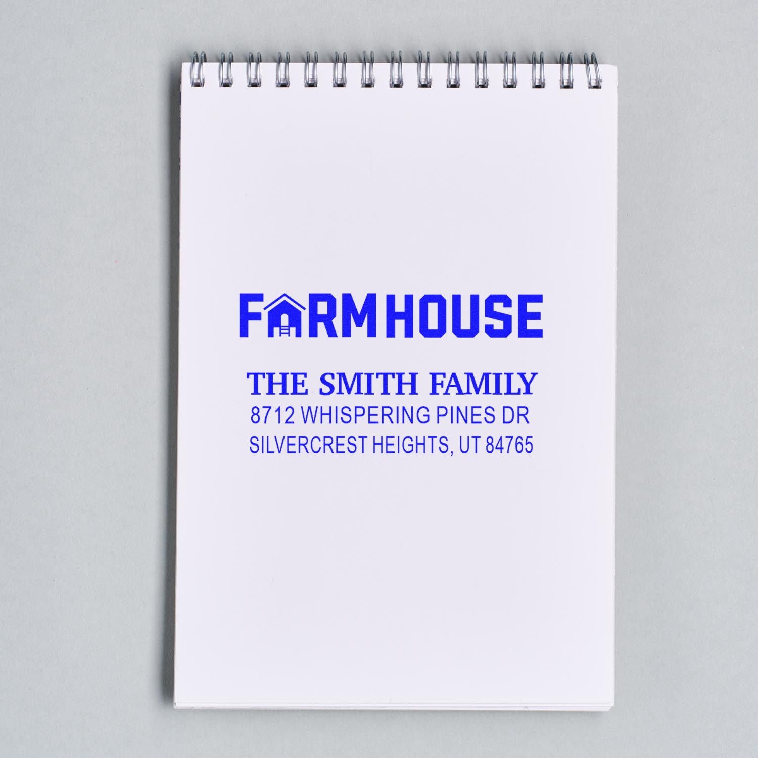 Blue farmhouse return address stamp impression on a spiral notebook, reading The Smith Family, 8712 Whispering Pines Dr, Silvercrest Heights, UT 84765.