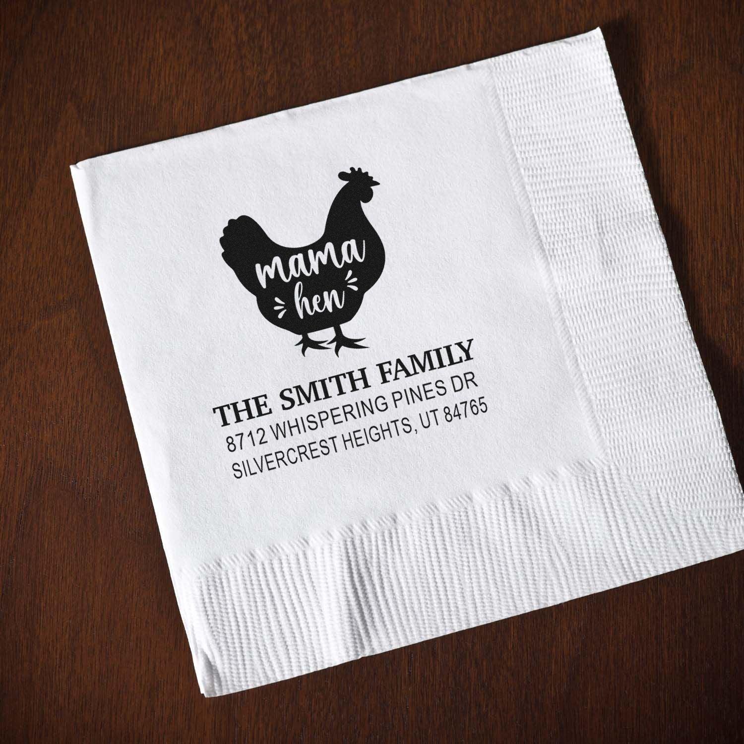Custom return address stamp on folded white napkin, featuring a mama hen design and The Smith Family details on a wooden table.