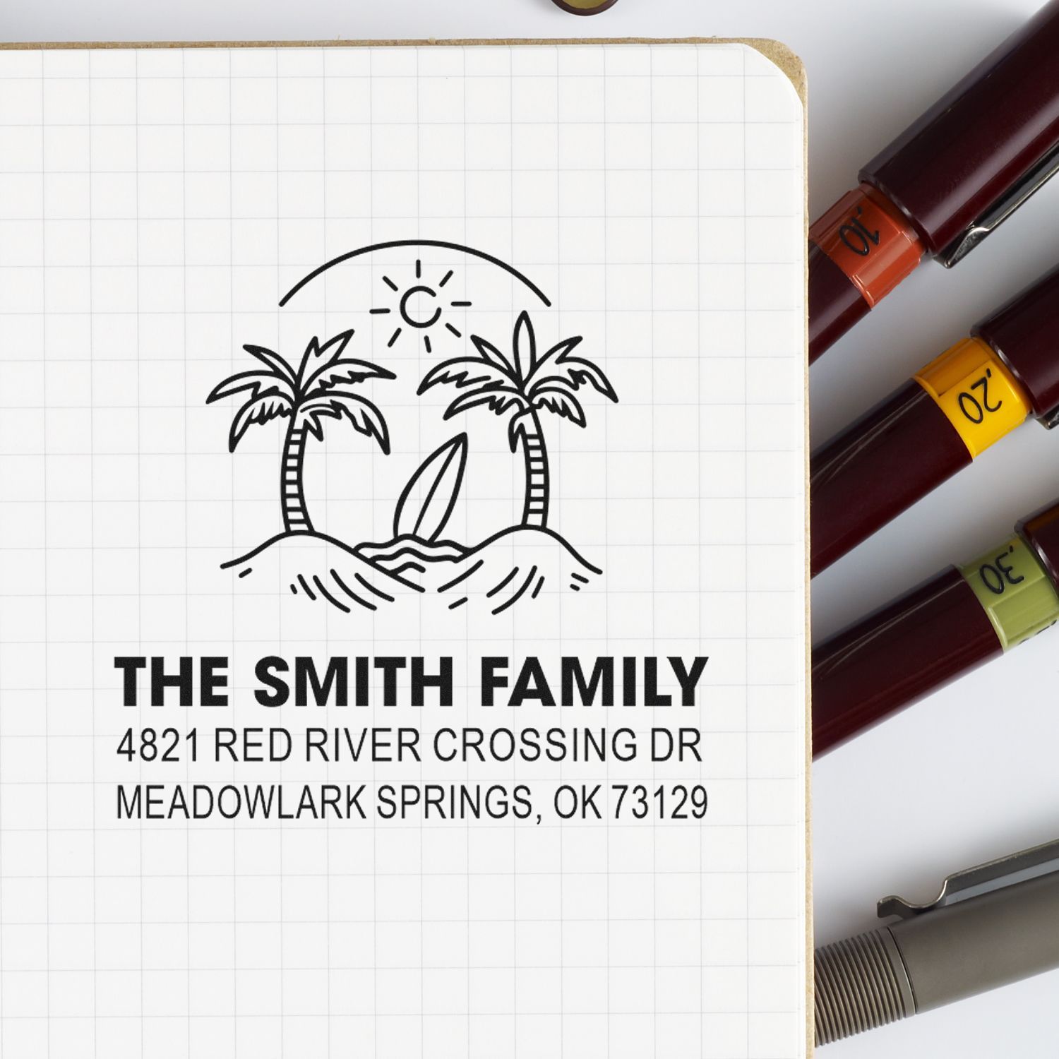 Custom address stamp for The Smith Family with palm tree beach design on graph notebook, beside ink stamp markers.