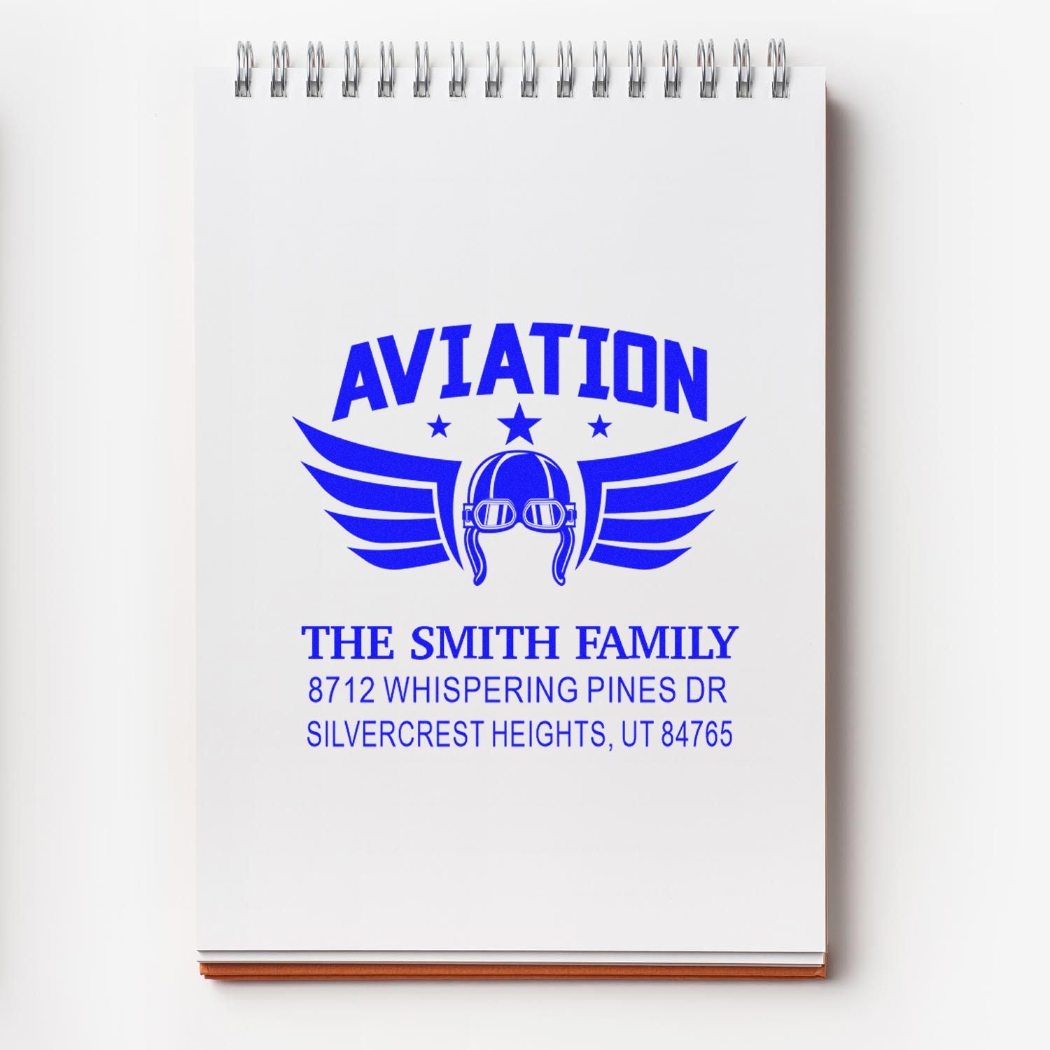 Custom aviation address stamp on a spiral notepad, featuring a blue winged pilot helmet design and The Smith Family address.