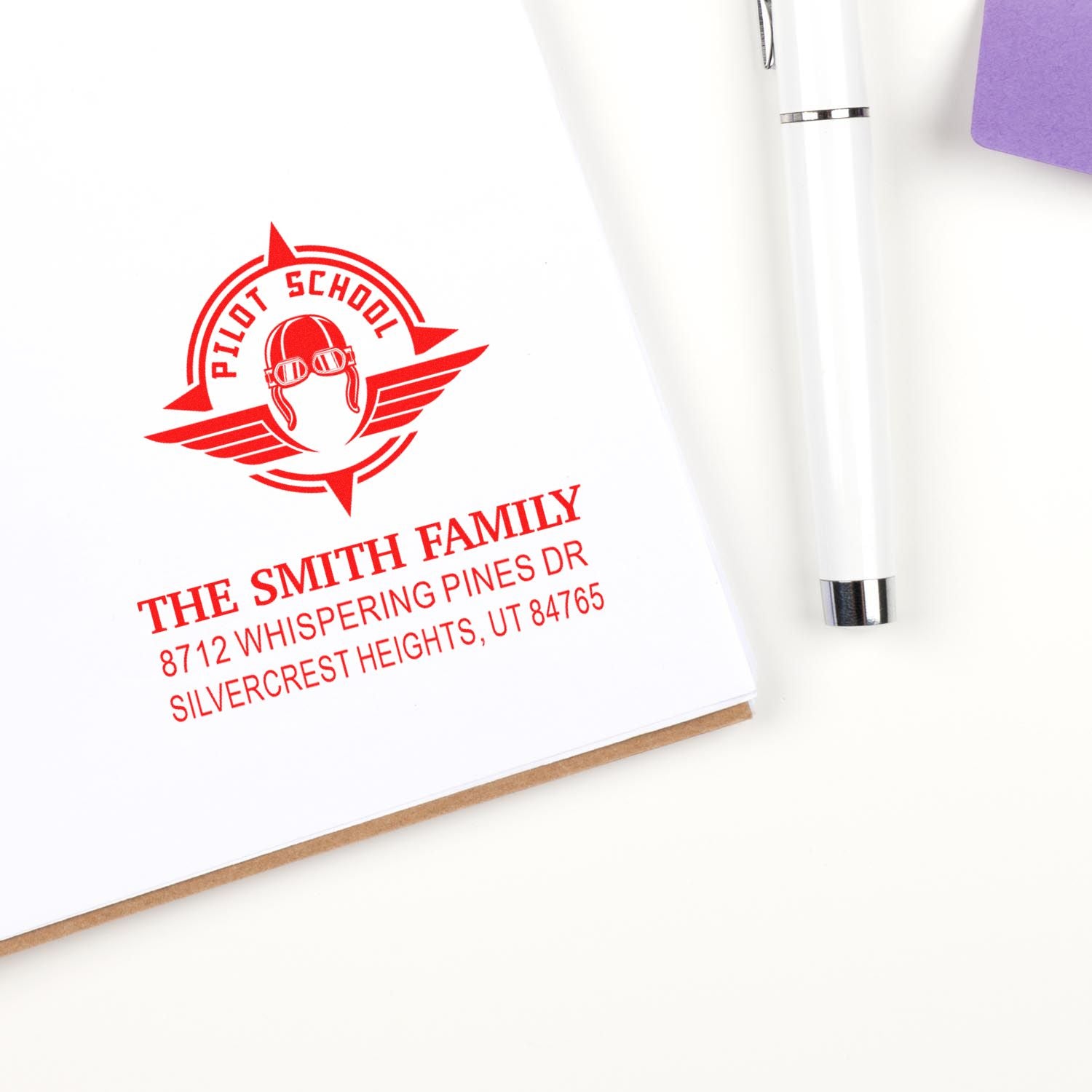 Custom red pilot school address stamp on white paper beside a white pen, featuring The Smith Family return address.