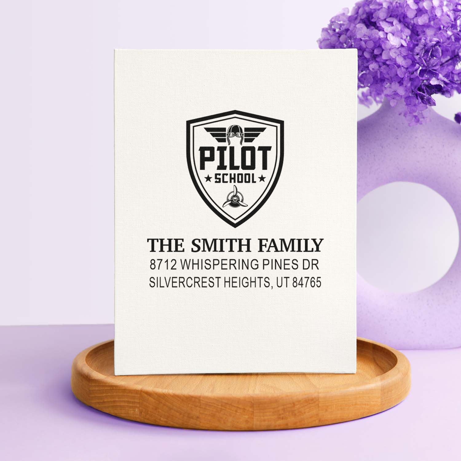 Personalized Pilot School return address stamp for The Smith Family, shown on a wooden stand with purple floral decor.