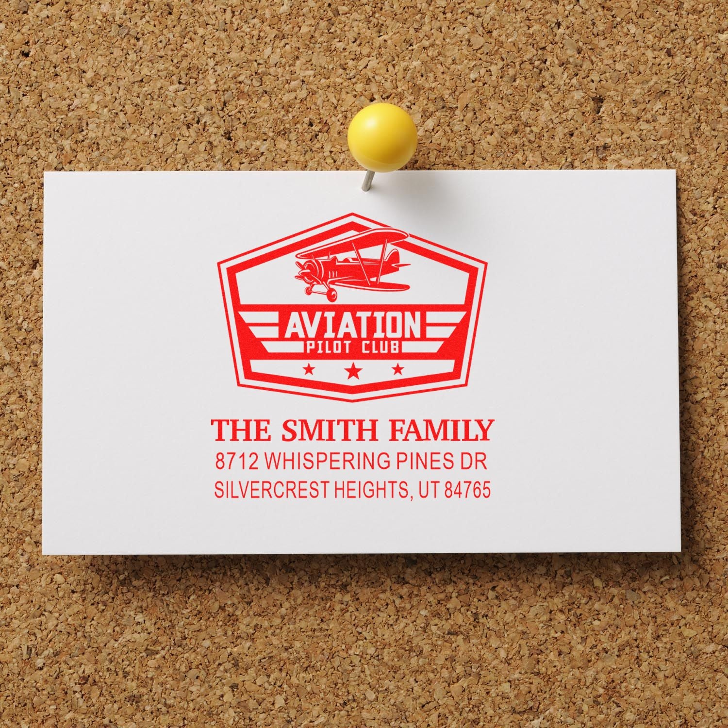 Custom aviation pilot club address stamp pinned on a corkboard, featuring a red biplane logo and The Smith Family name.