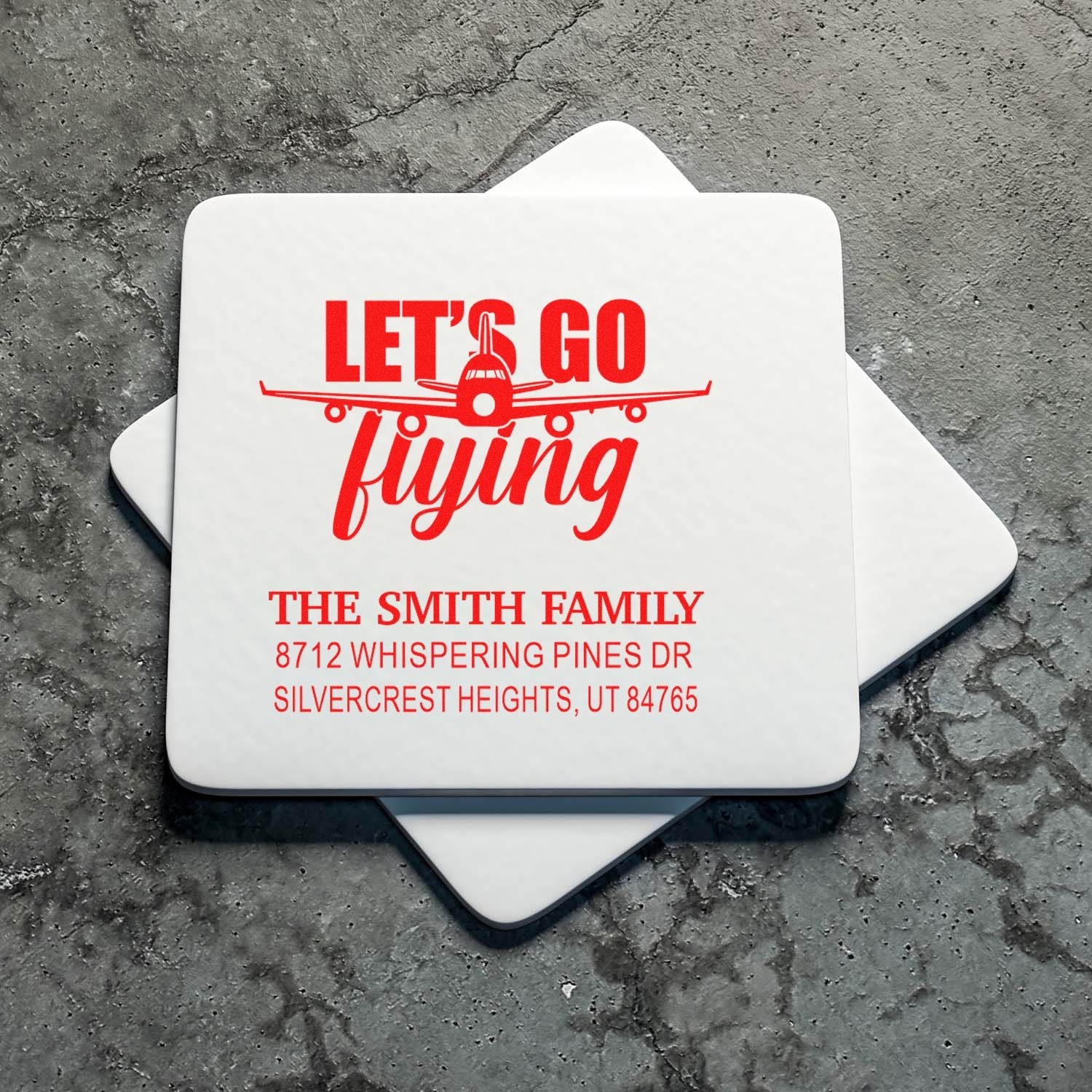 Custom address stamps with red Lets Go flying airplane design and The Smith Family return address on a gray stone background.