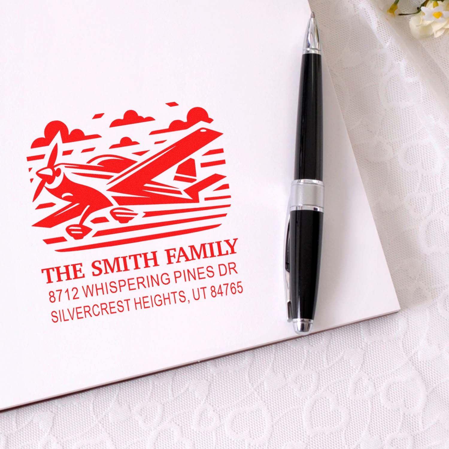 Custom red airplane family address stamp on white card with black pen, featuring The Smith Family and Silvercrest Heights, UT address.