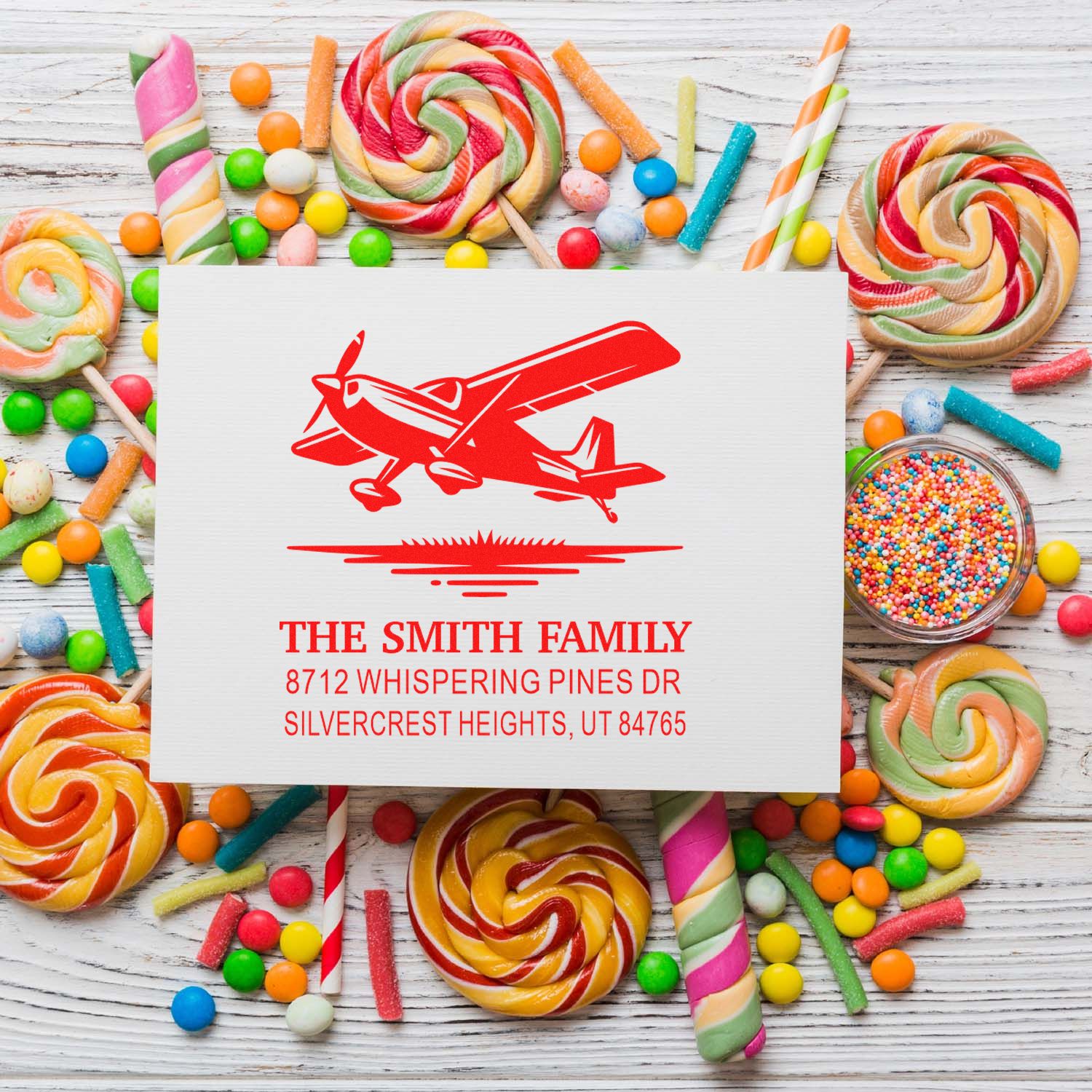 Custom airplane address stamp for The Smith Family on a white card, surrounded by colorful candy lollipops on a rustic wood background.