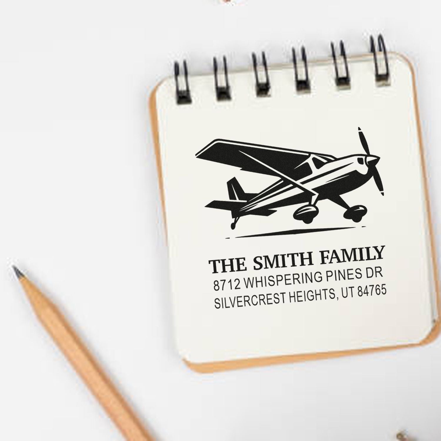Custom airplane return address stamp on a spiral notepad with pencil, featuring The Smith Family and home address.