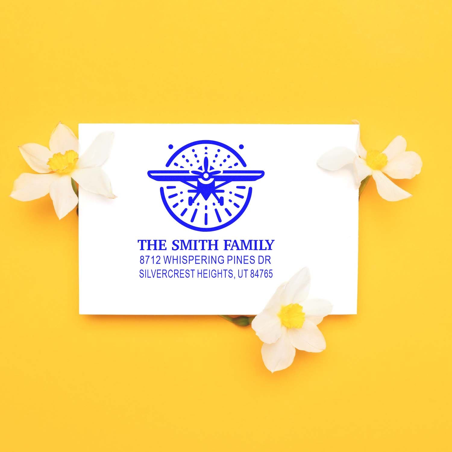 Personalized blue family address stamp with airplane logo on white card, styled with white flowers on a yellow background.