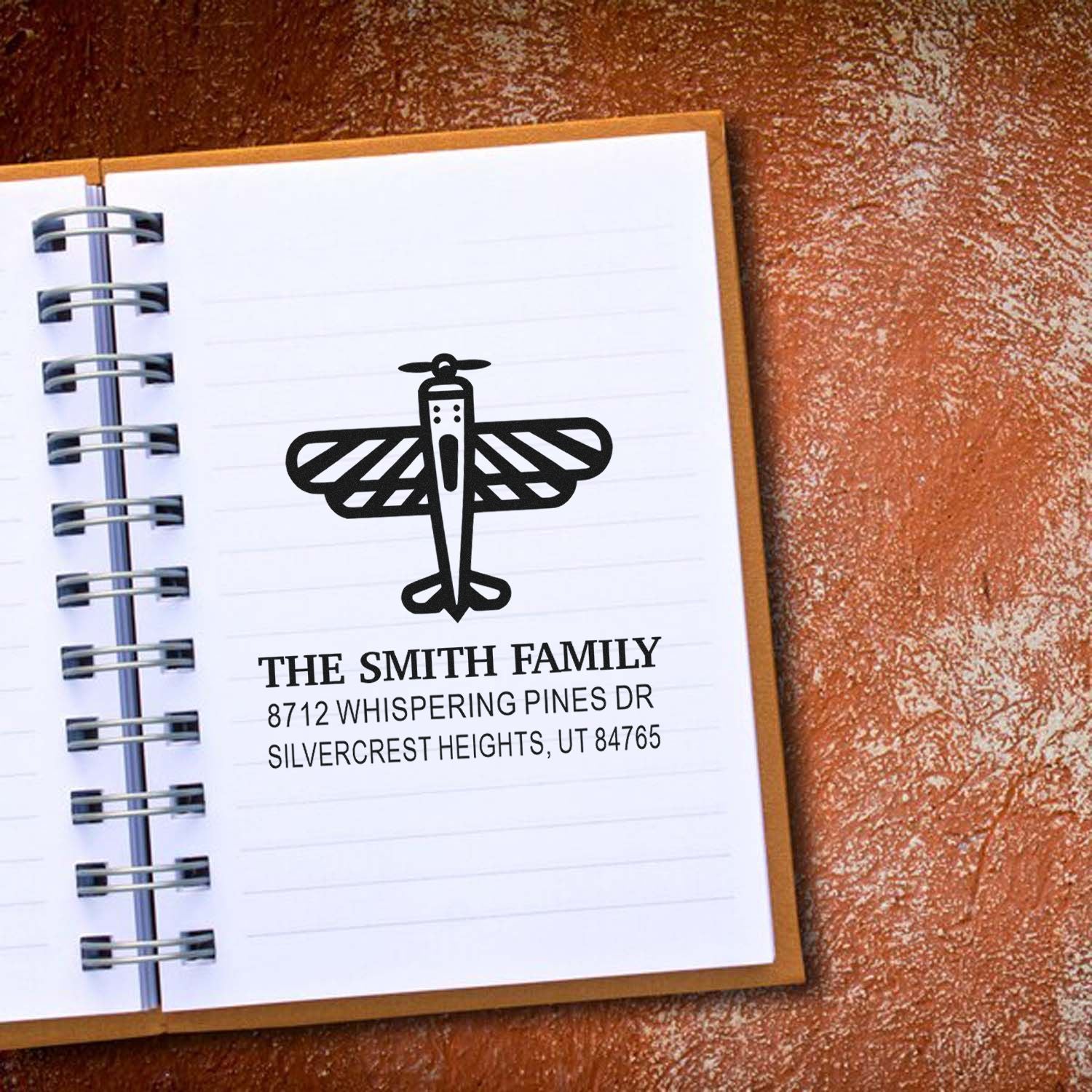 Custom family address stamp with dragonfly design on spiral notebook, reading The Smith Family and a Utah address.