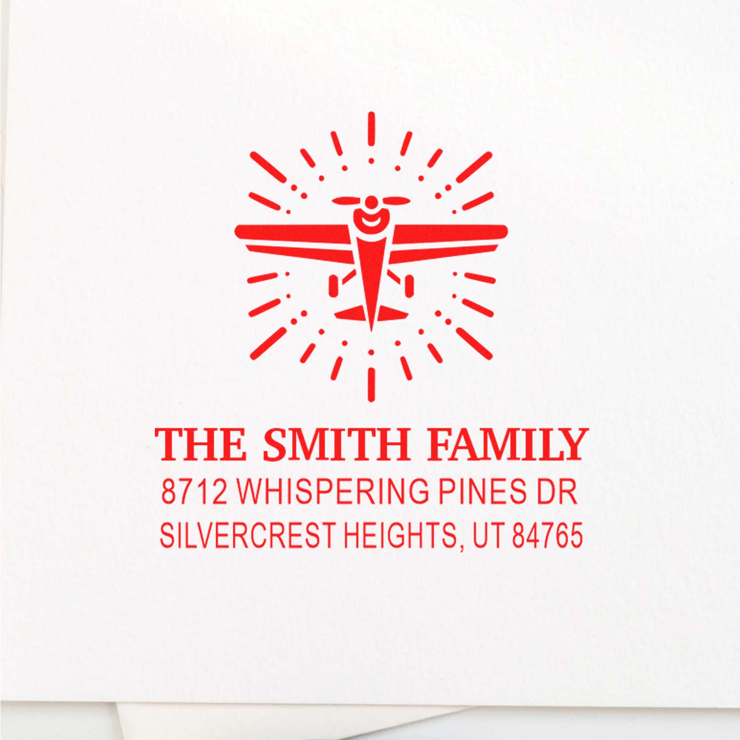 Red personalized family address stamp with airplane logo, reading The Smith Family, Whispering Pines Dr, Silvercrest Heights, UT 84765.
