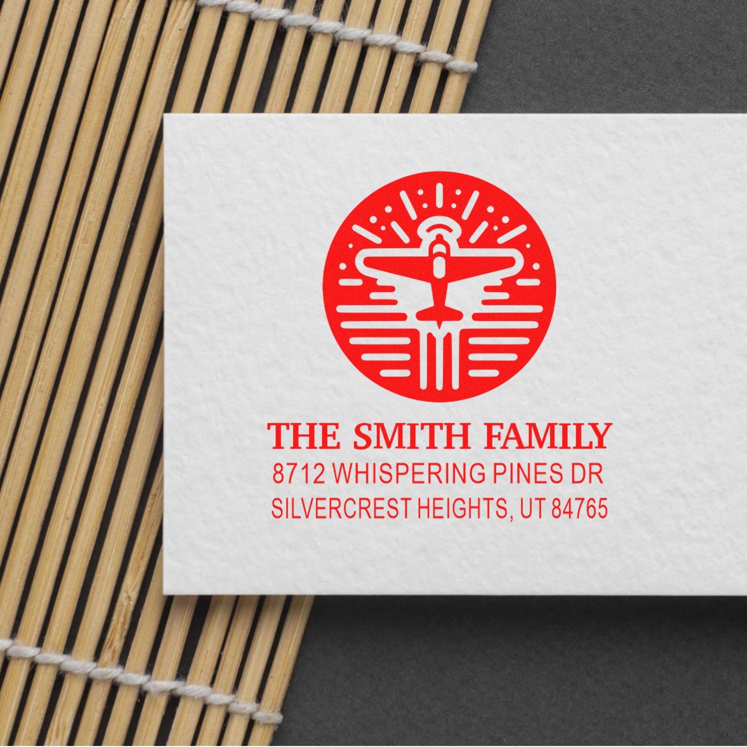 Custom personalized address stamp with red airplane logo for The Smith Family, shown on white paper over a bamboo mat background.