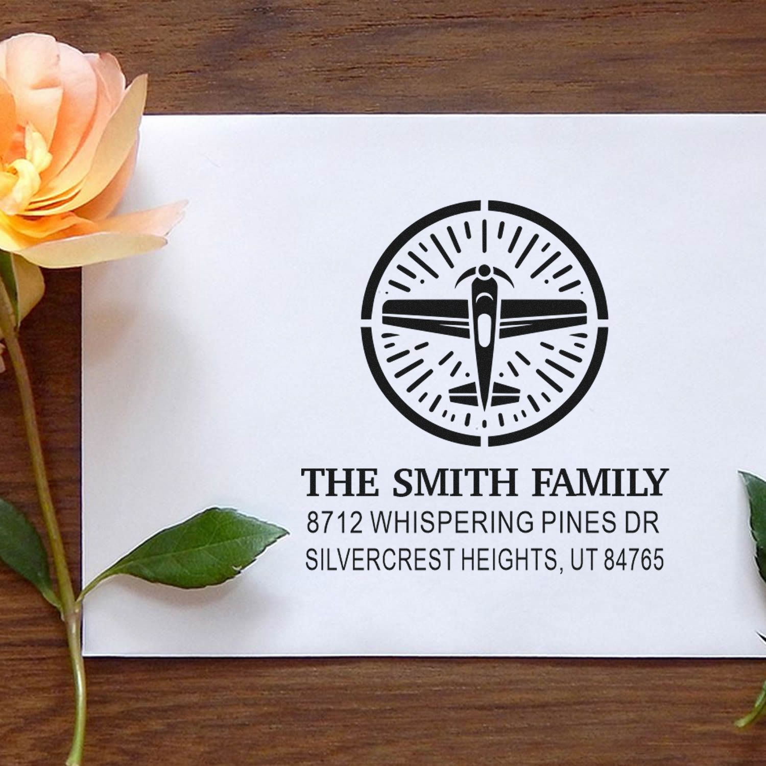 Personalized address stamp with airplane emblem for The Smith Family, displayed on a white card with flowers on a wooden table.