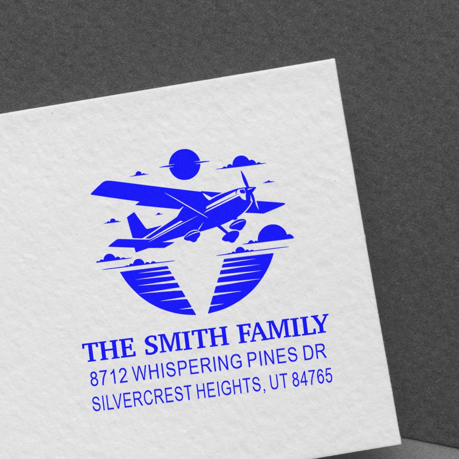 Personalized blue family address stamp with airplane logo and sunset clouds on white paper, featuring THE SMITH FAMILY and Silvercrest Heights, UT address.