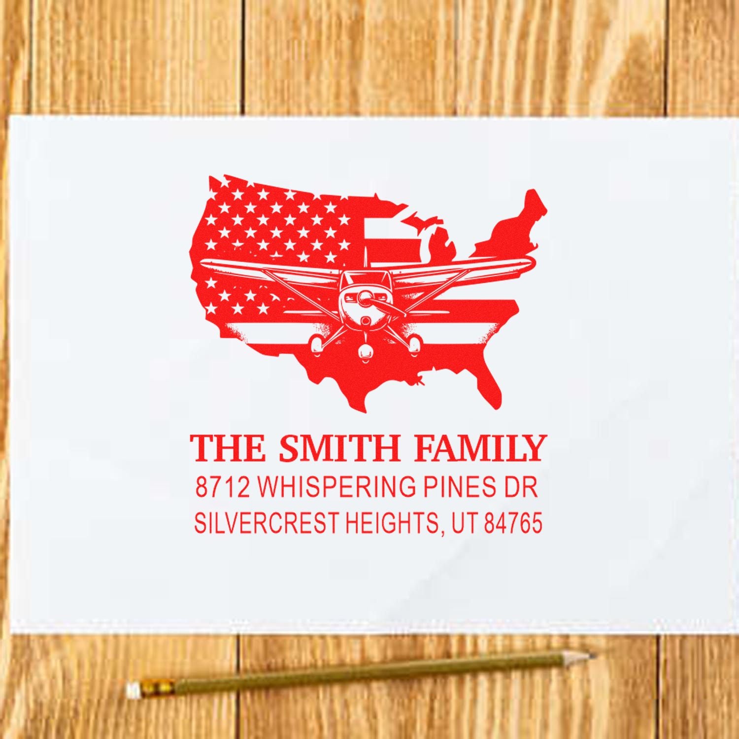 Personalized red address stamp with USA map and airplane design, reading The Smith Family, on white paper over a wooden table.