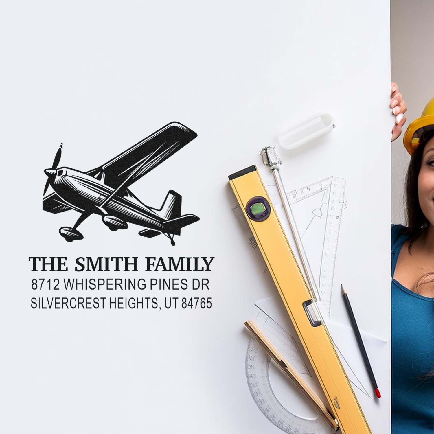 Custom return address stamp with airplane logo for The Smith Family, shown on a white board with drafting tools and a woman in a hard hat.