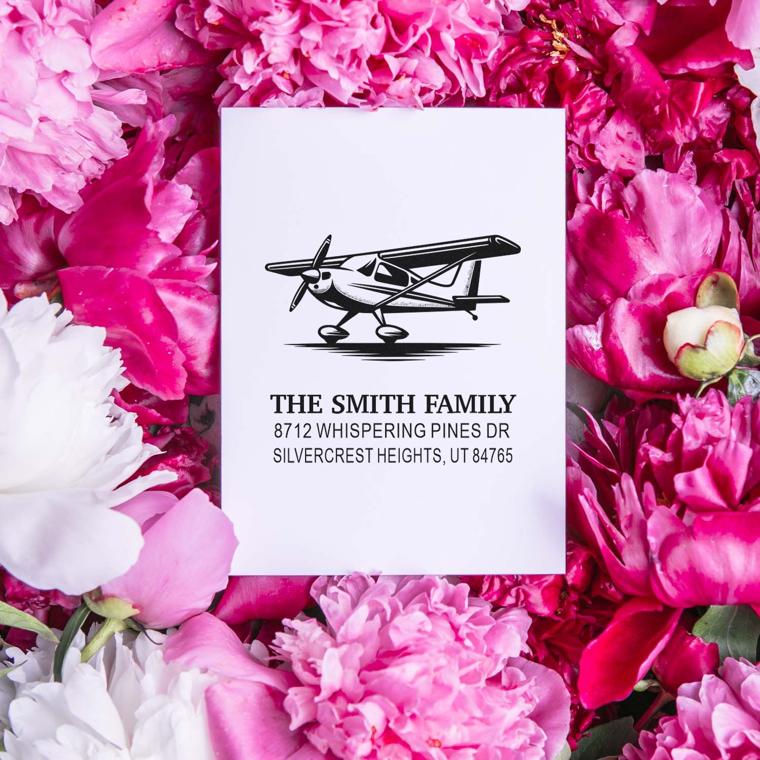 Personalized airplane return address stamp on white card, surrounded by pink peonies, featuring The Smith Family and a Utah address.