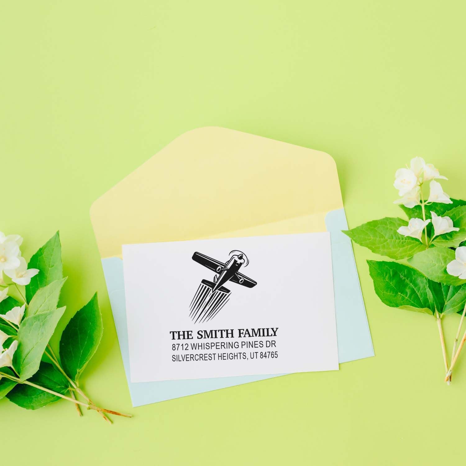 Personalized airplane address stamp for The Smith Family on pastel envelopes, styled with green leaves and white flowers on a lime background.