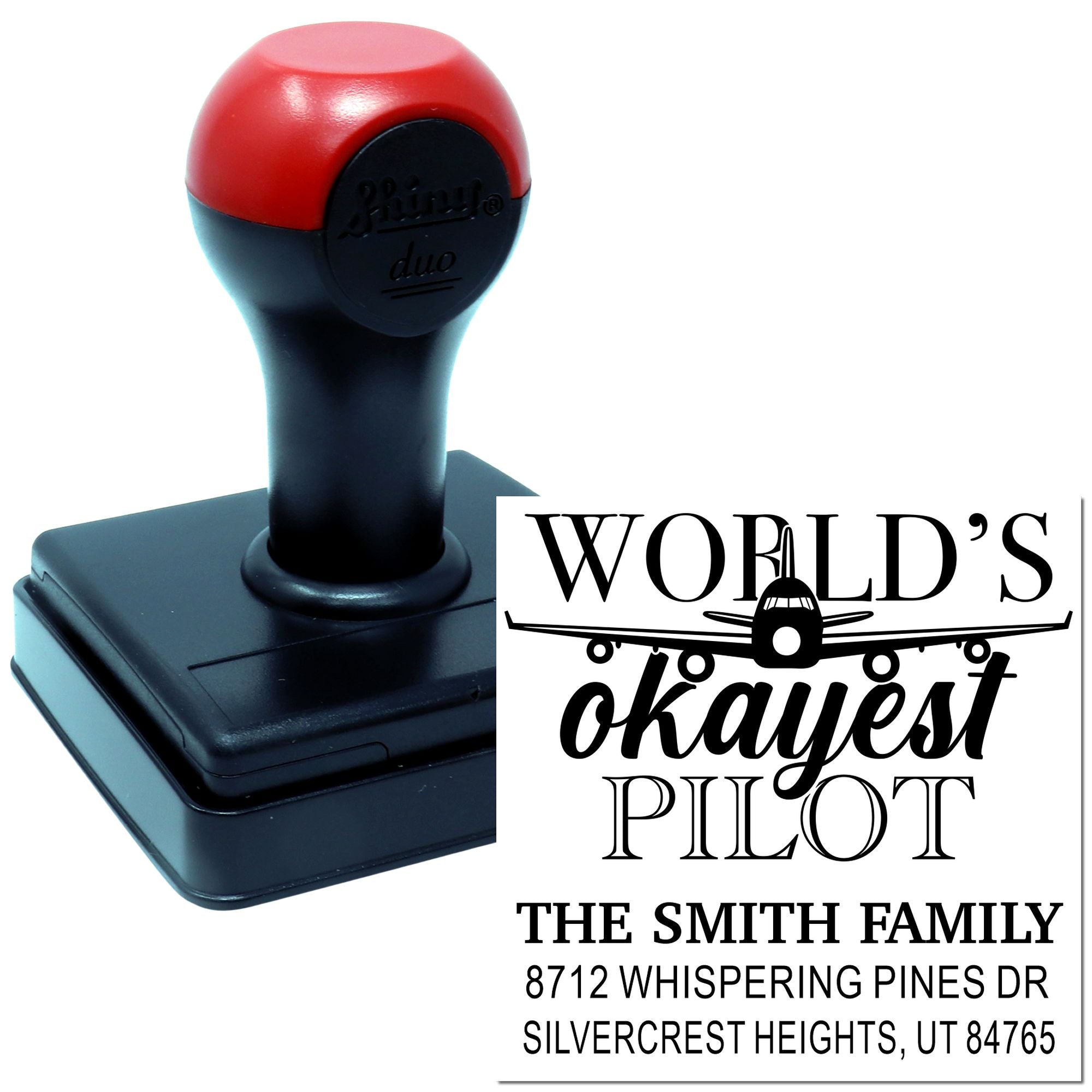 Custom self-inking stamp with red-and-black handle, showing a sample imprint for Worlds Okayest Pilot and a family address design.