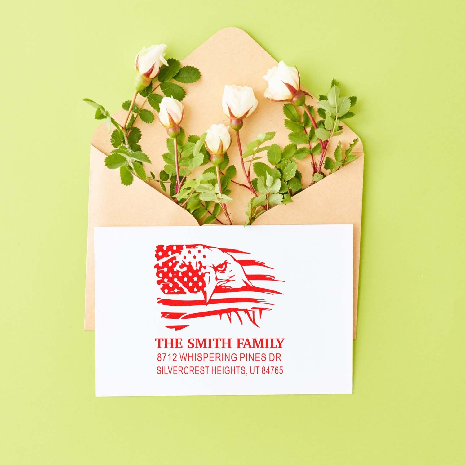 Custom family return address stamp set displayed on an envelope with white rose stems, red eagle design, and lime-green background.