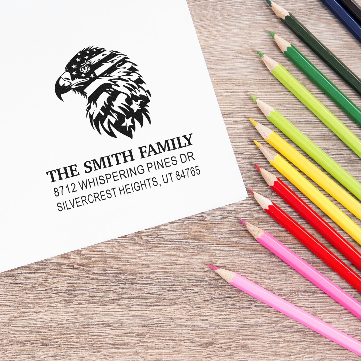 Personalized family address stamp with eagle design on paper, ????? with colorful pencils on a wood desk.