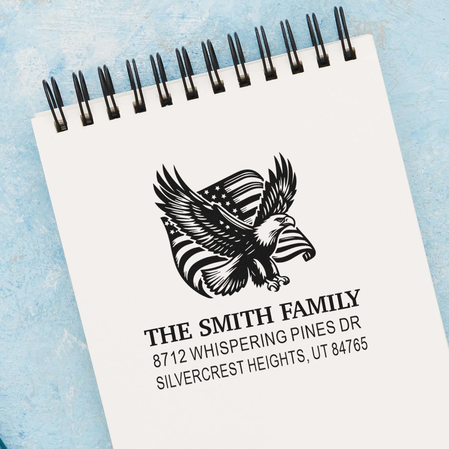 Custom self-inking address stamp with eagle and American flag design on a spiral notepad, featuring The Smith Family name and Utah address.