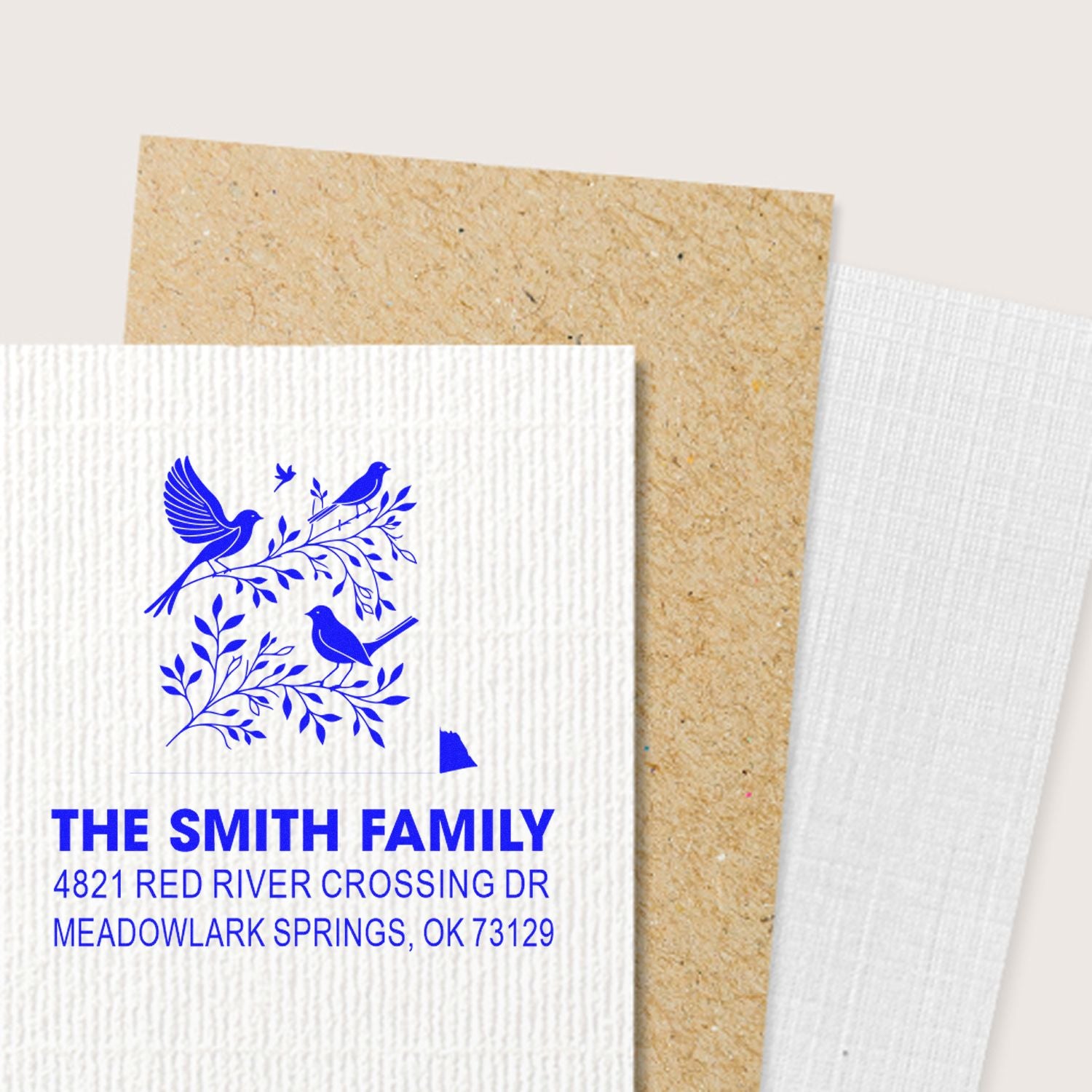 Custom family address rubber stamp with blue birds and leafy branches on textured paper, featuring The Smith Family and Meadowlark Springs, OK 73129