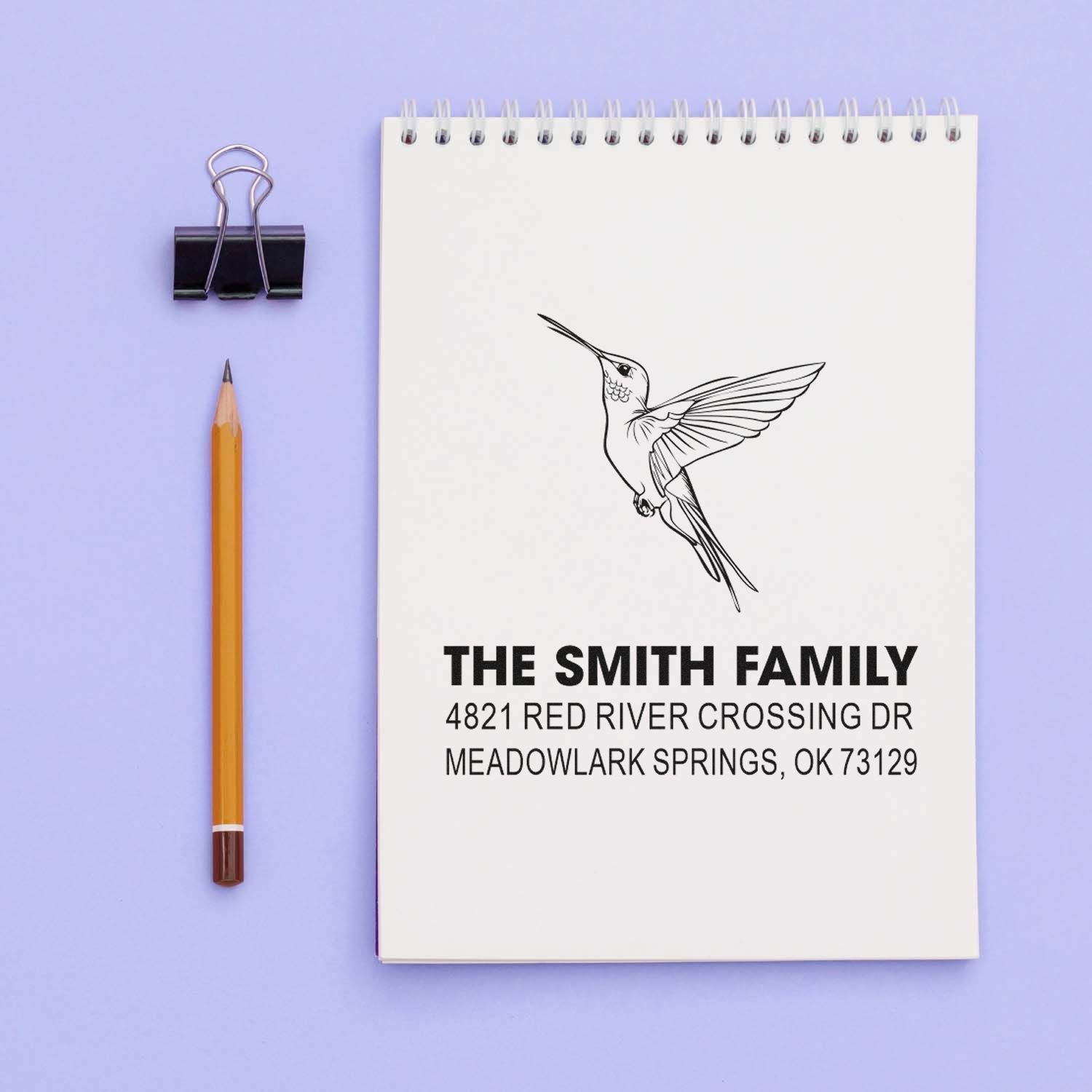 Personalized hummingbird return address rubber stamp with The Smith Family name and Meadowlark Springs, OK address on a spiral notebook mockup.