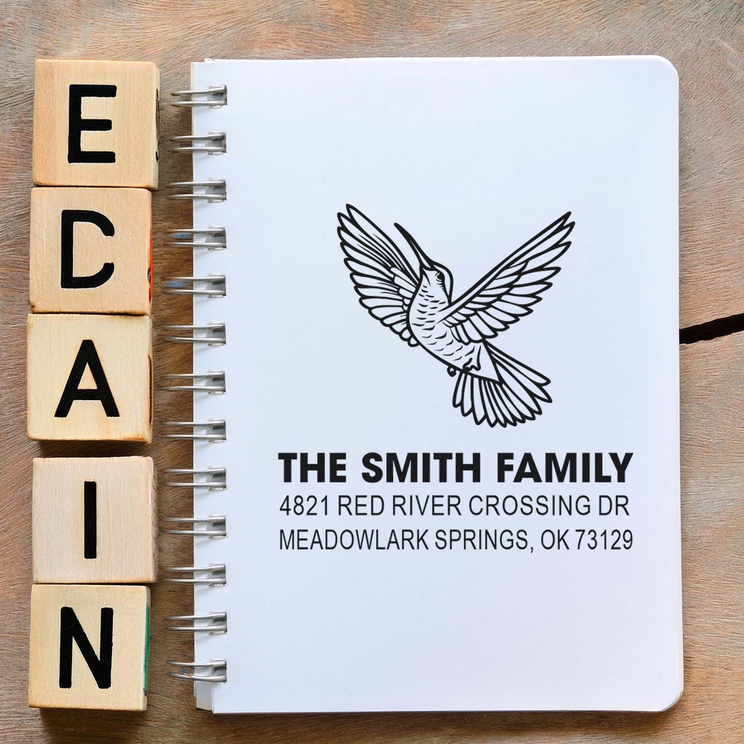 Wooden alphabet stamp blocks beside a custom hummingbird return address rubber stamp with family name, street address and notebook design.