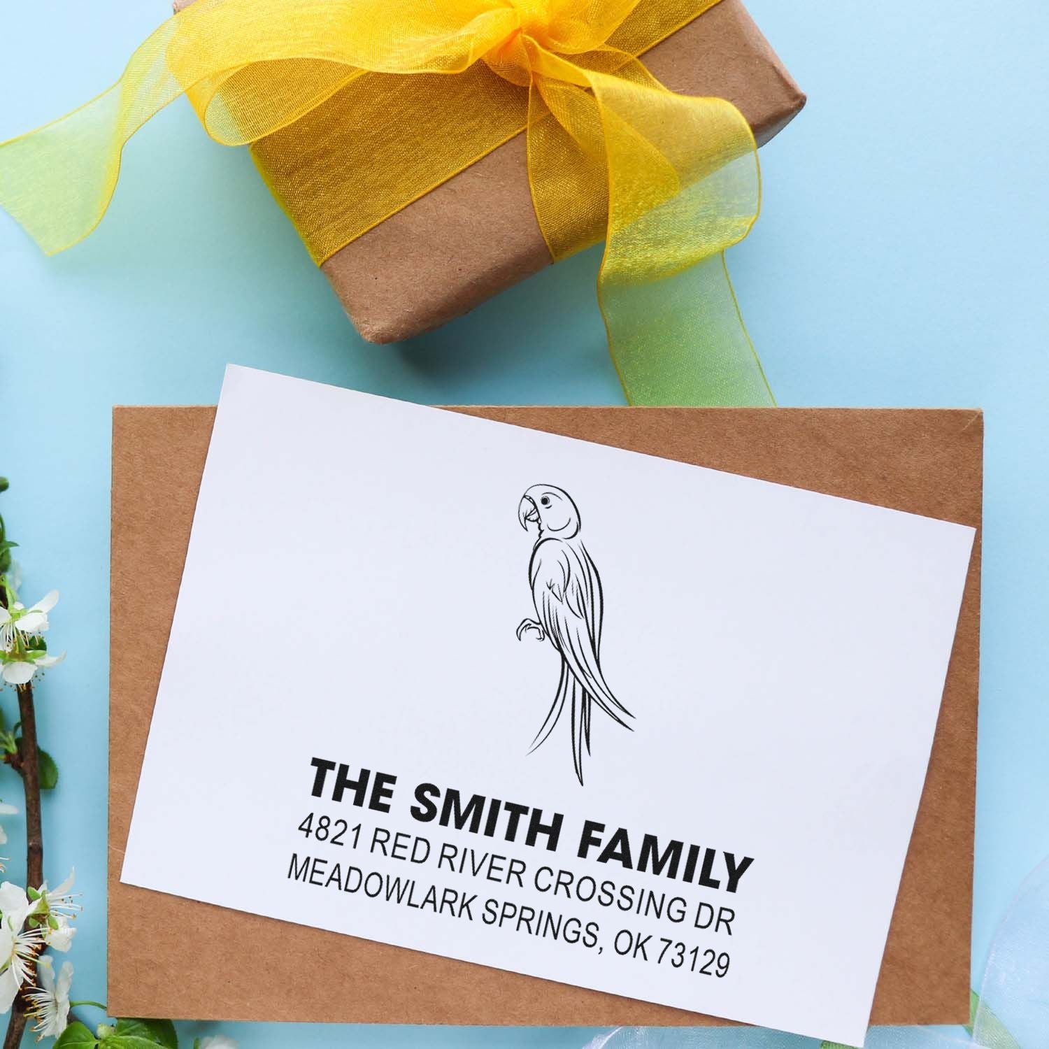 Custom rubber return address stamp with parrot design on white card over kraft envelope and gift box, featuring The Smith Family mailing details.