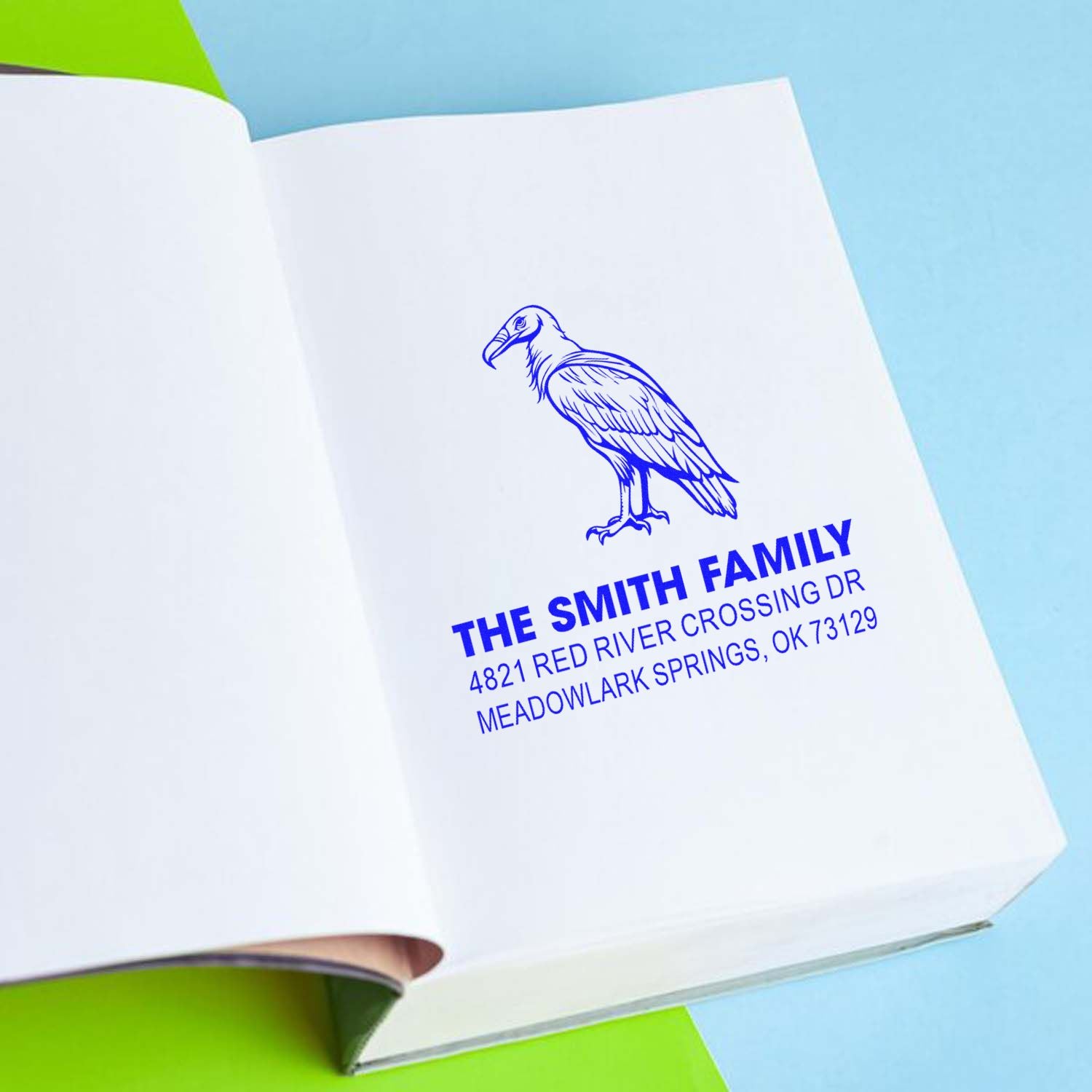 Custom rubber address stamp with a blue bird illustration, family name, and return address printed on a white notebook page.